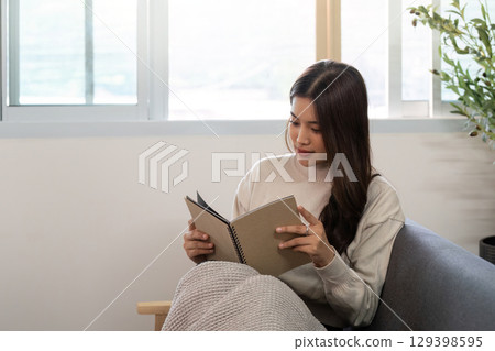Reading and Relaxation. Young woman reading a notebook in a cozy living room. Reading and Relaxation. Young woman reading a notebook in a cozy living room. 129398595