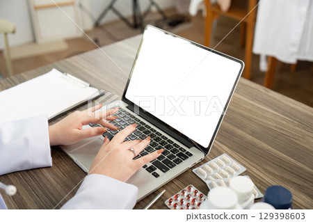Telemedicine Workflow. A doctor typing on a laptop during a patient consultation. 129398603
