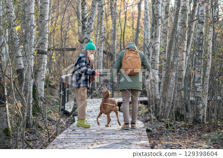 Active backpacking family plays fetch with Vizsla dog while hiking eco trail in autumn birch grove Active backpacking family plays fetch with Vizsla dog while hiking eco trail in autumn birch grove 129398604
