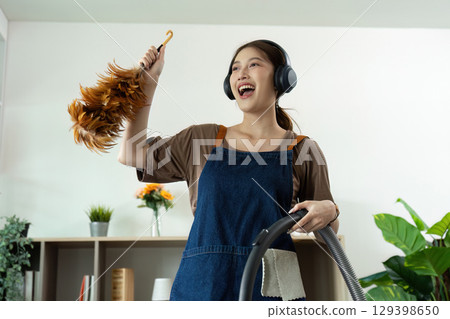 Home Cleaning. Happy woman singing while vacuuming, enjoying music during chores. 129398650