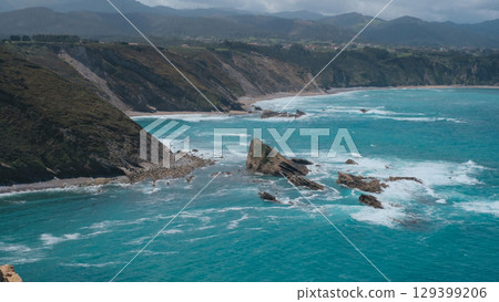 A scenic aerial or high-angle shot of a rugged coastline with turquoise blue waters crashing against rocky shores and cliffs. Asturias, Spain 129399206