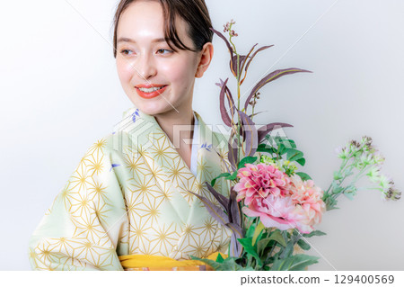 一個穿著和服的女人拿著一朵花 129400569