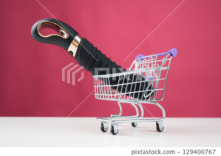 Sex toy in miniature shopping cart on pink background.  129400767