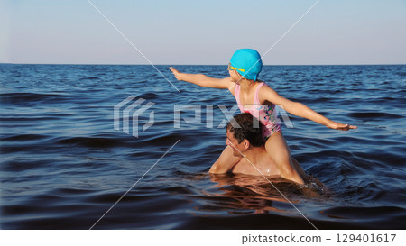 Father carrying daughter on shoulders while playing in sea 129401617