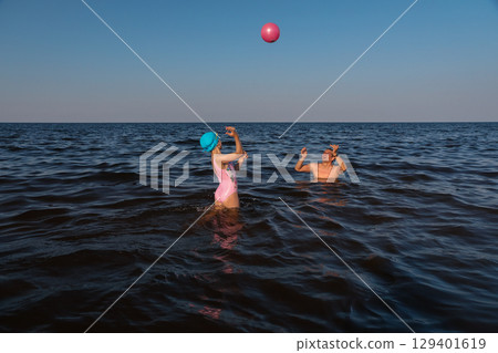 Father and daughter playing with ball in sea on sunny day 129401619