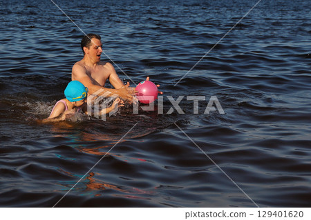 Dad and daughter are happily playing ball in water and swimming 129401620
