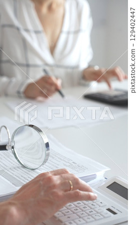 Group of accountants are working together, using a magnifying glass and a calculator, to audit financial reports in office. Audit and taxes in business Group of accountants are working together, using a magnifying glass and a calculator, to audit financial reports in office. Audit and taxes in business 129402447