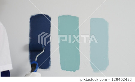 Painter wearing protective gloves rolling blue paint on white wall, creating gradient color effect for home interior renovation project Painter wearing protective gloves rolling blue paint on white wall, creating gradient color effect for home interior renovation project 129402453