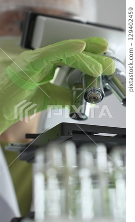 Close up of green gloved hands of a scientist adjusting a microscope in a laboratory, emphasizing the significance of scientific research and analysis. Medicine, healthcare and science concept 129402459