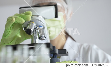 Gloved scientist adjusting a microscope, conducting research in a laboratory setting, surrounded by scientific equipment. Medicine, healthcare and science concept 129402482