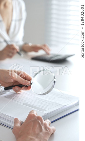 Team of accountants are working together, using a magnifying glass and a calculator, to audit financial reports in office. Audit and taxes concept 129402601