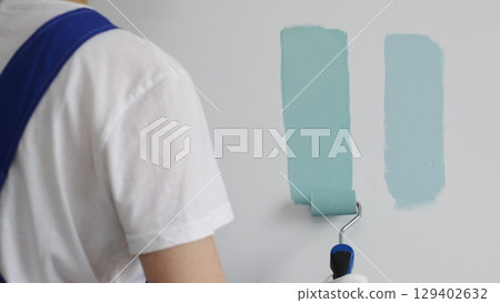 Professional painter holding paint roller, comparing light green paint shades, selecting precise wall color for home renovation, ensuring ideal interior design aesthetic 129402632