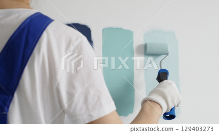 Painter wearing protective gloves rolling blue paint on white wall, creating gradient color effect for home interior renovation project Painter wearing protective gloves rolling blue paint on white wall, creating gradient color effect for home interior renovation project 129403273