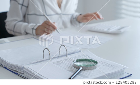 Magnifying glass on financial documents, with an accountant using a calculator and taking notes, emphasizing accounting, finance, and tax preparation. Audit and taxes concept 129403282