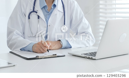 Female doctor documents patient information while working with digital devices at workplace in office. Medicine and healthcare concept 129403296