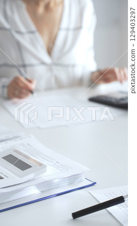 Close up of a calculator on financial documents, with an accountant taking notes, emphasizing accounting, finance, and tax preparation. Audit and taxes in business Close up of a calculator on financial documents, with an accountant taking notes, emphasizing accounting, finance, and tax preparation. Audit and taxes in business 129403297