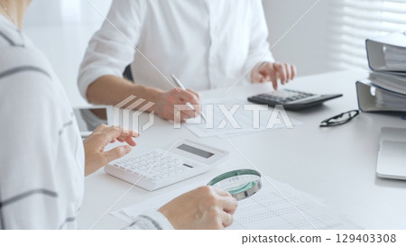 Groupe of accountants collaborating on financial analysis, using a magnifying glass, calculator, and laptop to ensure data accuracy. Audit and taxes 129403308