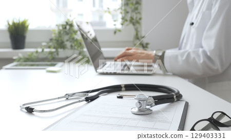 Stethoscope over a medical records are lying on the desk opposite the doctor is typing on a laptop with a in a medical office, suggesting online healthcare or telemedicine services. Medicine concept 129403331