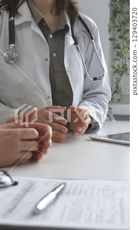 Doctor woman in medical coat is explaining diagnosis to male patient during a medical consultation in a medical office, gesturing with hands, vertical close up view. Medicine and health care 129403720