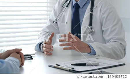 Male doctor explaining diagnosis, gesturing with hand to patient during consultation in clinical setting. Medicine and healthcare concept Male doctor explaining diagnosis, gesturing with hand to patient during consultation in clinical setting. Medicine and healthcare concept 129403722