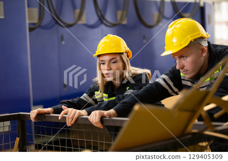 Male and female factory workers wearing safety gear checking cardboard waste in industrial bin. Team analyzing recycling process or material inspection in manufacturing site. Male and female factory workers wearing safety gear checking cardboard waste in industrial bin. Team analyzing recycling process or material inspection in manufacturing site. 129405309