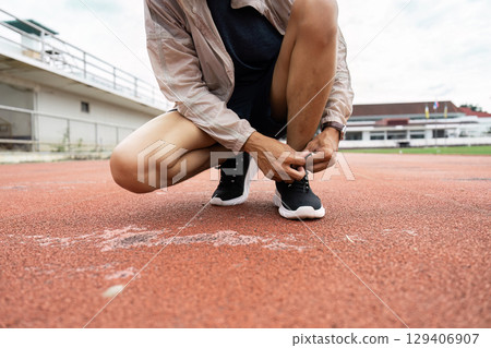 Athletic preparation runner tying shoelaces on track outdoor stadium action shot dynamic environment close-up perspective Athletic preparation runner tying shoelaces on track outdoor stadium action shot dynamic environment close-up perspective 129406907