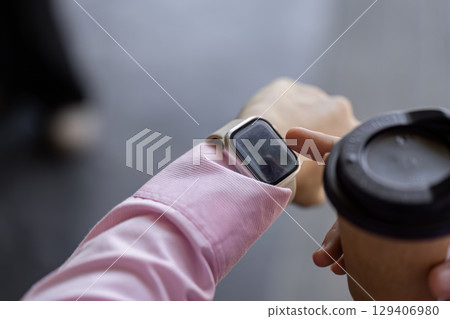 Checking notifications on smartwatch while holding coffee in office environment with modern technology and casual attire 129406980