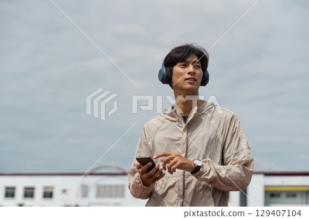 Young Man in Sportswear Listening to Music While Exercising Outdoors on a Cloudy Day 129407104