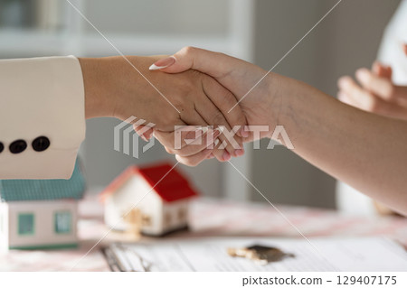 Real Estate Agent Shaking Hands with Client Over Contract and Model House on Table 129407175