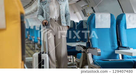 Traveler with Luggage Walking Down Airplane Aisle in Casual Attire, Ready for Journey, Inside Modern Aircraft Cabin with Blue Seats Traveler with Luggage Walking Down Airplane Aisle in Casual Attire, Ready for Journey, Inside Modern Aircraft Cabin with Blue Seats 129407480