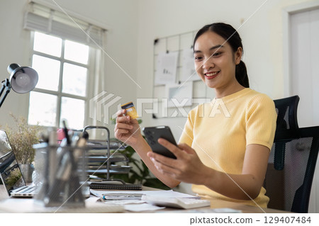 Young Woman Managing Finances at Home with Smartphone and Credit Card for Effective Savings and Budget Planning 129407484