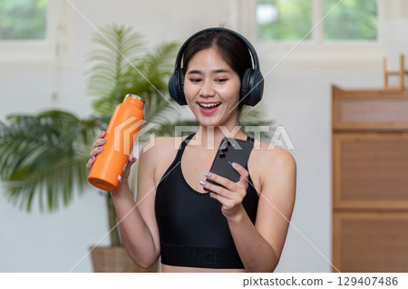 Young Woman Enjoying a Wellness Routine with Music and Hydration in a Modern Home Setting 129407486