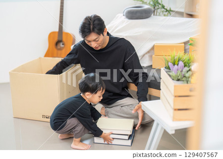 Father and child organizing books and plants in a cozy living space 129407567