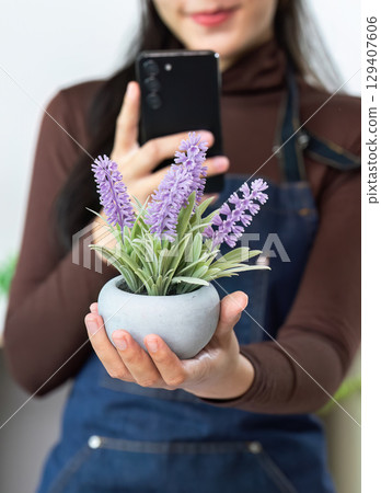 Florist presenting beautiful plant with smartphone 129407606