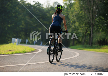 Woman cyclist riding bike in summer park 129410025