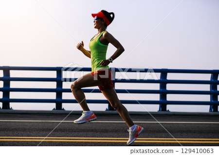 Fitness asian woman runner running on seaside bridge 129410063