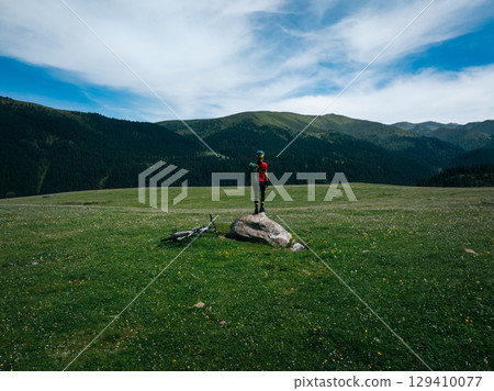 Aerial view of woman cyclist with mountain bike on flowering grassland mountain Aerial view of woman cyclist with mountain bike on flowering grassland mountain 129410077