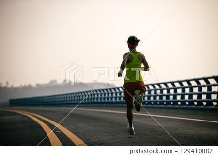 Fitness asian woman runner running on seaside bridge 129410082