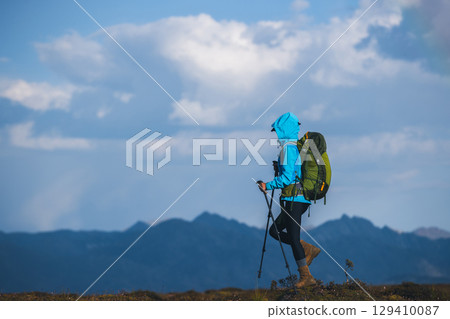 Backpacking woman hiking on sunset high altitude mountain top 129410087