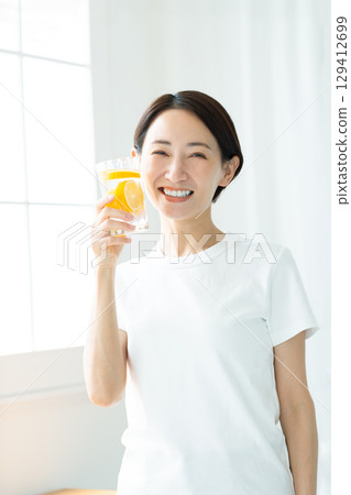 一位年輕女子,笑容燦爛,手捧一杯檸檬水,上身 一位年輕女子,笑容燦爛,手捧一杯檸檬水,上身 129412699