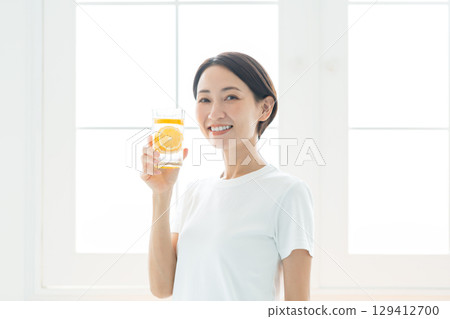 一位年輕女子,笑容燦爛,手捧一杯檸檬水,上身 一位年輕女子,笑容燦爛,手捧一杯檸檬水,上身 129412700