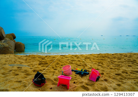 Baby bucket, water gun and diving mask on the beach against the azure sea Baby bucket, water gun and diving mask on the beach against the azure sea 129413307