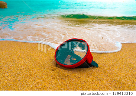 A diving mask lies on a sandy beach and is washed by waves of water 129413310