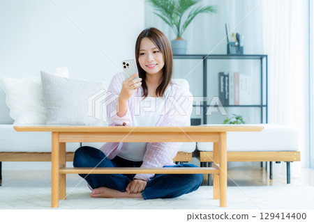 A young woman operating a smartphone in a room 129414400