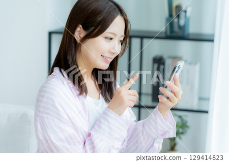 A young woman operating a smartphone in a room A young woman operating a smartphone in a room 129414823