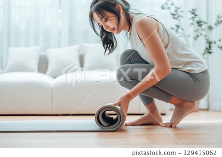 Young Asian woman doing yoga, twisting on a mat in the living room at home Young Asian woman doing yoga, twisting on a mat in the living room at home 129415062