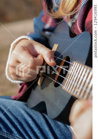 Close up of female hands playing guitar ukulele and singing relaxing enjoying outdoors on sunny autumn day. Hippie woman in boho style training playing musical instrument. Fall leaves Close up of female hands playing guitar ukulele and singing relaxing enjoying outdoors on sunny autumn day. Hippie woman in boho style training playing musical instrument. Fall leaves 129416995