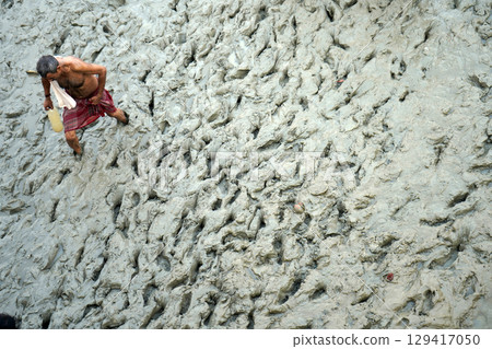 14th October 2023, Babughat, Kolkata, West Bengal, India. Man Walking Through Muddy Terrain with a Bottle 129417050