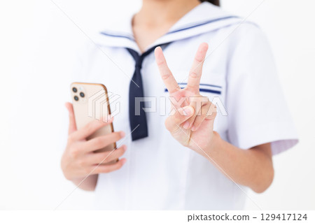 一名身穿夏季校服的國中女生拿著智慧型手機做出和平手勢 129417124