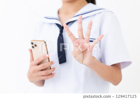 一名身穿夏季校服的國中女生拿著智慧型手機，用四根手指向上指 129417125